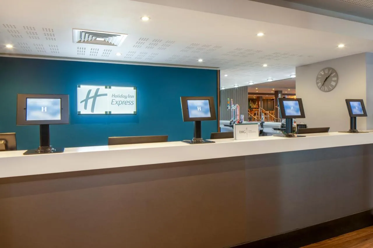 a lobby with a counter with three monitors on it at Holiday Inn Express Birmingham - Snow Hill by IHG in Birmingham